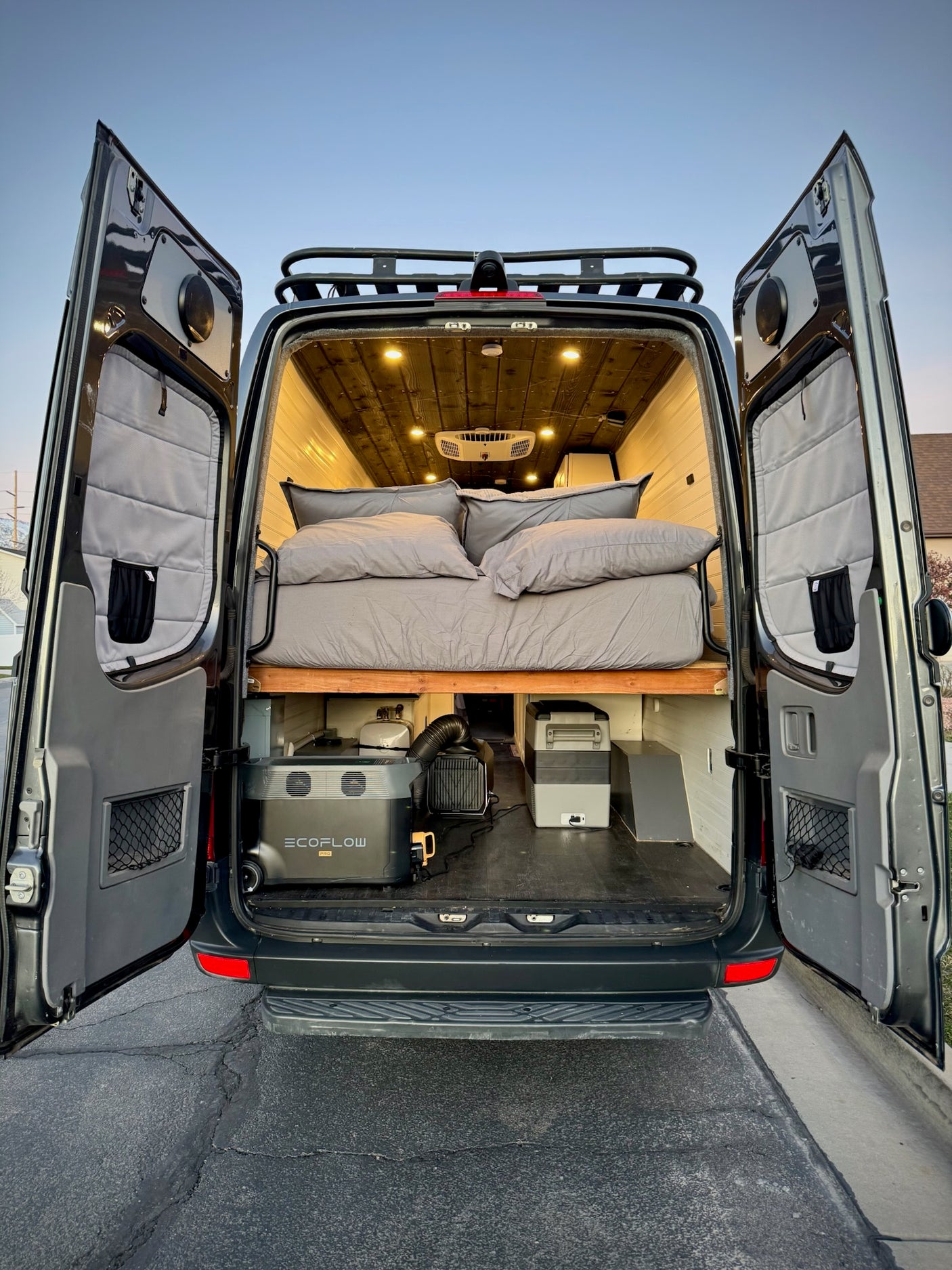 Experience an RV rental! Rear view of a camper van with open doors, revealing a comfy bed & portable power. Ready for adventure.