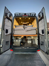 Experience an RV rental! Rear view of a camper van with open doors, revealing a comfy bed & portable power. Ready for adventure.