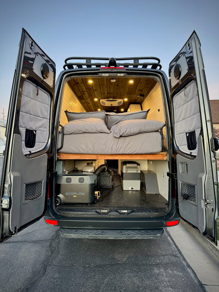 Experience an RV rental! Rear view of a camper van with open doors, revealing a comfy bed & portable power. Ready for adventure.