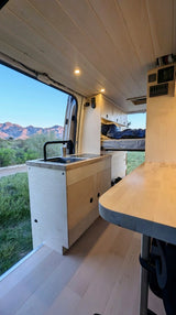 Modern RV rental interior with kitchen, sink, and bed, featuring wood accents and scenic mountain views.