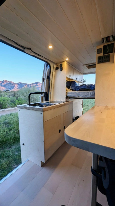 Modern RV rental interior with kitchen, sink, and bed, featuring wood accents and scenic mountain views.