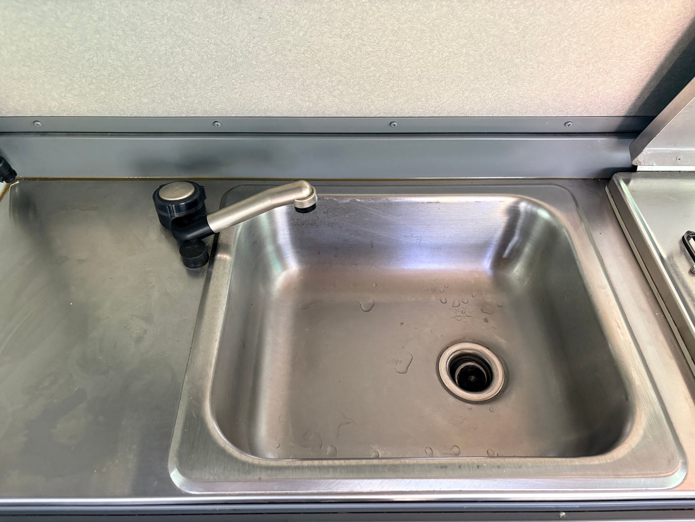 RV rental kitchen: compact stainless steel sink with faucet on a metal counter, featuring visible water droplets.