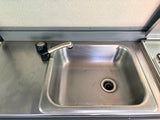 RV rental kitchen: compact stainless steel sink with faucet on a metal counter, featuring visible water droplets.