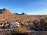 White RV rental van camping in a desert landscape with mountains and a bright blue sky.