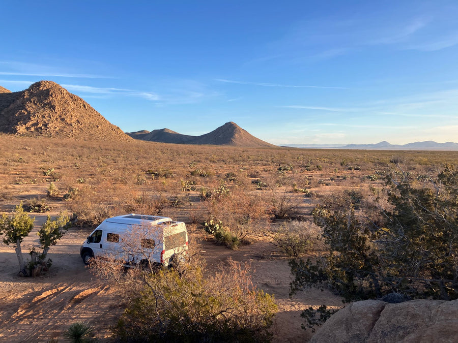 White RV rental van camping in a desert landscape with mountains and a bright blue sky.