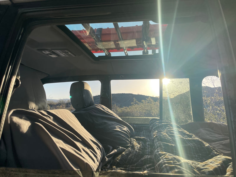 Inside an RV rental camper: cozy bedding with a plaid blanket, bright mountain view, and sunlight through the sunroof. — photo 18
