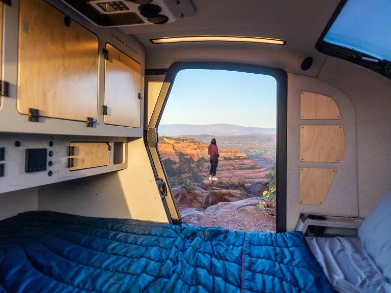 An RV rental provides a cozy bed with epic views! A person looks out at red rock canyons from inside a camper.