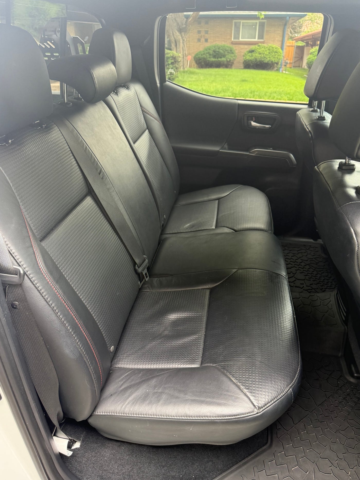 Rear interior of a comfortable RV rental vehicle: black leather seats, headrests, & textured floor mats. View outside through window. — photo 11