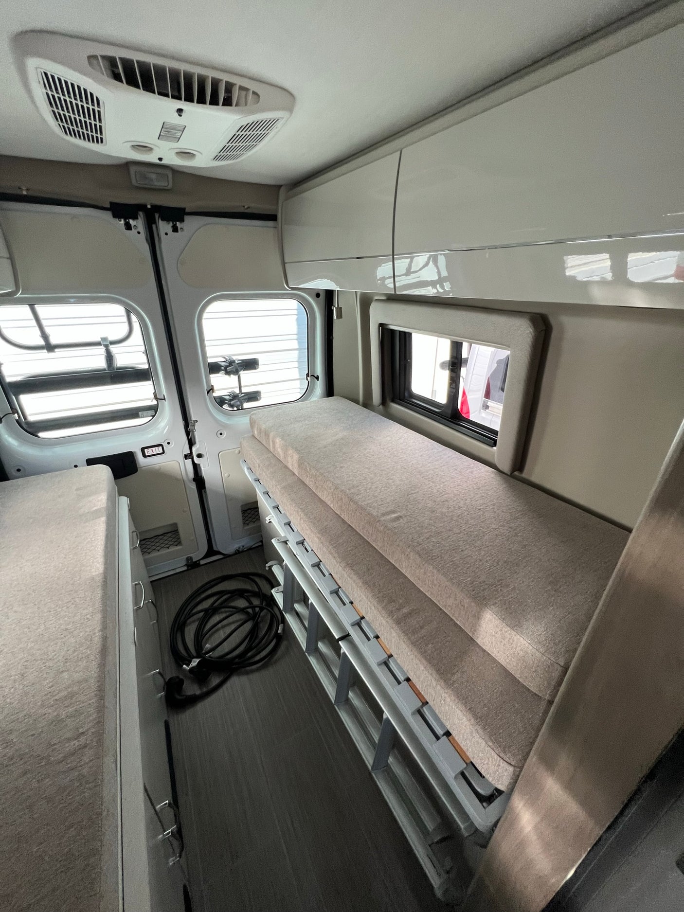 Clean RV rental interior: two sleeping areas (bunk beds on right), overhead storage, and ceiling AC for comfort.