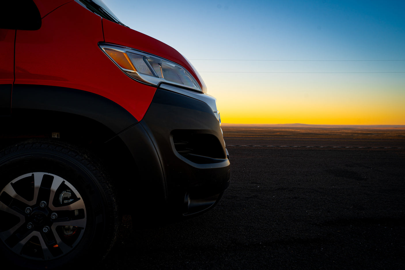 The front of a red RV rental parked overlooking a vast landscape at golden hour, promising travel adventure.