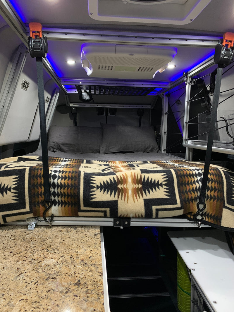 RV rental interior: A suspended bed with a patterned blanket, overhead AC, and blue lighting, maximizing space. — photo 11