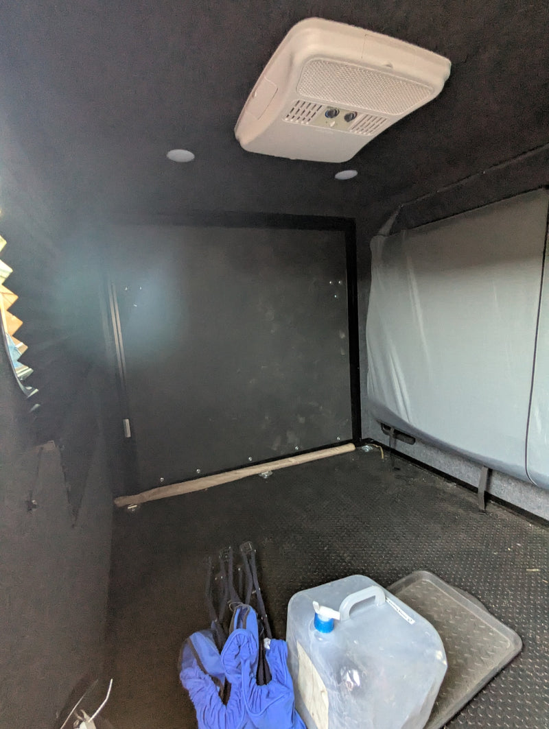 Compact RV rental interior with AC unit, storage, and water jug. Ideal for mobile living and travel. — photo 6