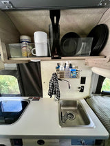 Inside this RV rental kitchen: compact sink, stovetop, and organized overhead storage with dishes and mugs.