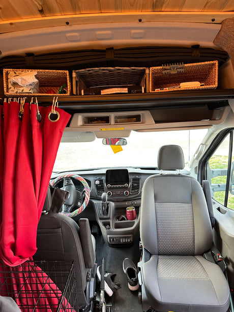 RV rental interior showing front cabin, seats, storage baskets, and red curtains for a cozy camper van experience.