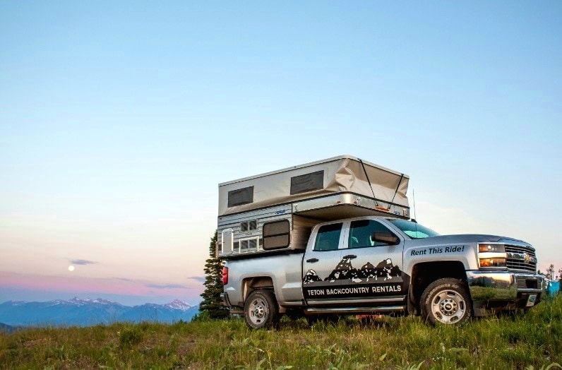 Teton Backcountry Rentals RV rental: A silver pickup truck with a pop-up camper on a scenic mountain hilltop at dusk. — photo 8