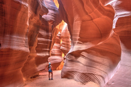 Woman stands amazed in a vibrant slot canyon, its swirling sandstone walls glowing from above. Start your RV rental journey here!