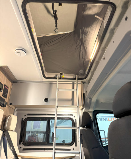 Interior of an RV rental: a ladder leads to a pop-top sleeping area. Features include controls and front seating.