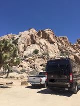 Joshua Tree National Park: An RV rental van and truck parked amidst massive desert rocks, with climbers exploring.