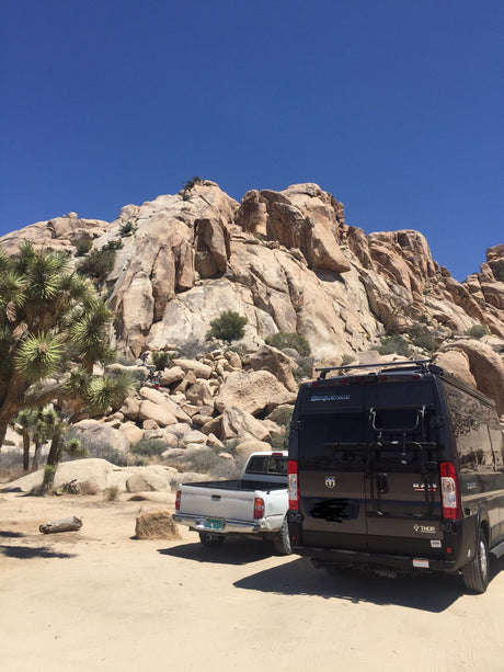Joshua Tree National Park: An RV rental van and truck parked amidst massive desert rocks, with climbers exploring.