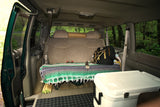 Inside an RV rental: a comfortable van interior with a bed-like seat, cooler, and outdoor gear.