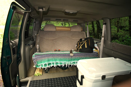 Inside an RV rental: a comfortable van interior with a bed-like seat, cooler, and outdoor gear.