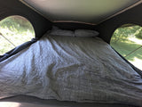 Inside an RV rental pop-top, a comfortable bed with grey bedding and pillows offers views of nature.