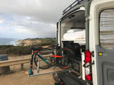 RV rental: custom van with bed, mountain bikes on a pull-out tray, and an outdoor oven by the scenic coast.