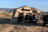 RV rental-style overland camping setup with a rooftop tent, trailer, and truck in a vast, sunny desert landscape.
