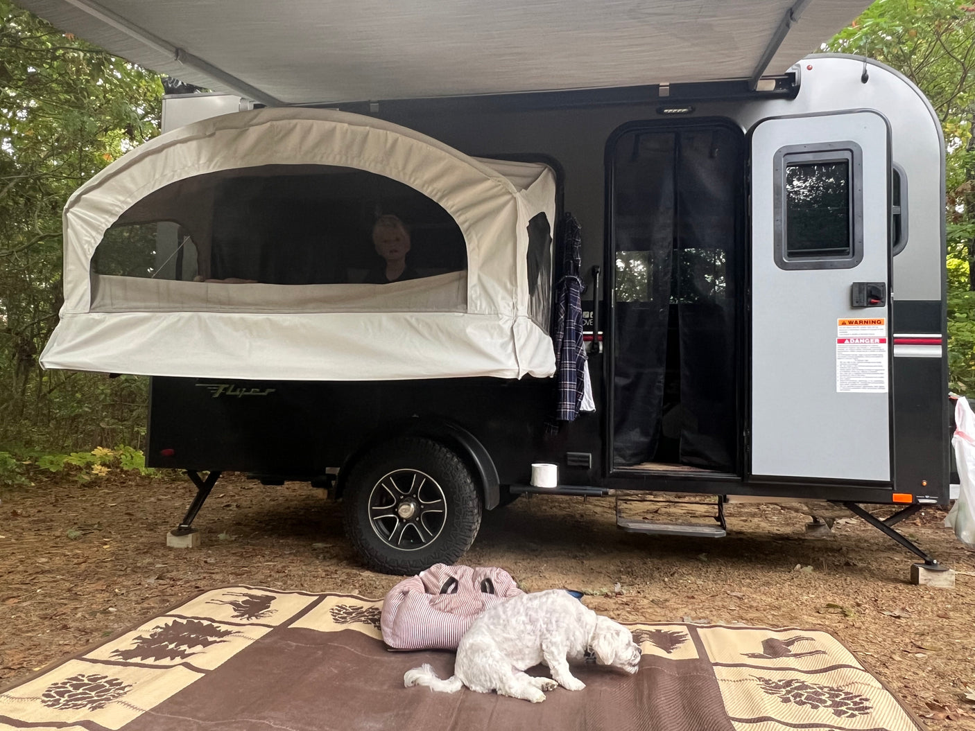 Enjoying the outdoors with an RV rental. Camper trailer with pop-out bed, child inside, dog resting on mat.