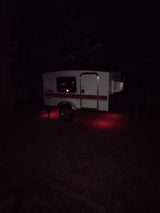 White RV rental camper glowing with red underlights at a dark campsite for your next outdoor adventure.