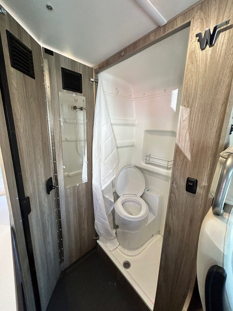 RV rental's compact wet bath: a white toilet inside a shower pan, with a shower curtain and wood-grain walls.