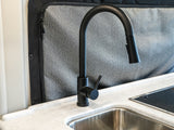 Sleek black faucet & stainless sink in a modern RV rental kitchen, featuring light counters & textured wall panel. Ready for your adventure.