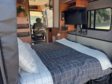 Inside a comfortable RV rental, featuring a cozy bed, TV, and a scenic view of the road from the window.