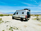 Silver rv rental van in a vast desert with mountains under a blue sky. A perfect rig for off-grid van life adventures.