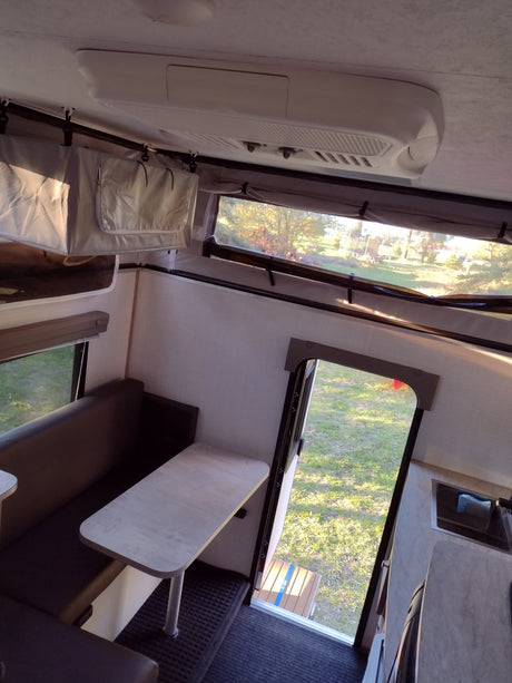 RV rental interior: dining booth, overhead AC, and large pop-up windows with outdoor views.