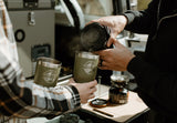 Two people pour steaming drinks into branded travel mugs, highlighting the convenient camp kitchen setup in an RV rental.