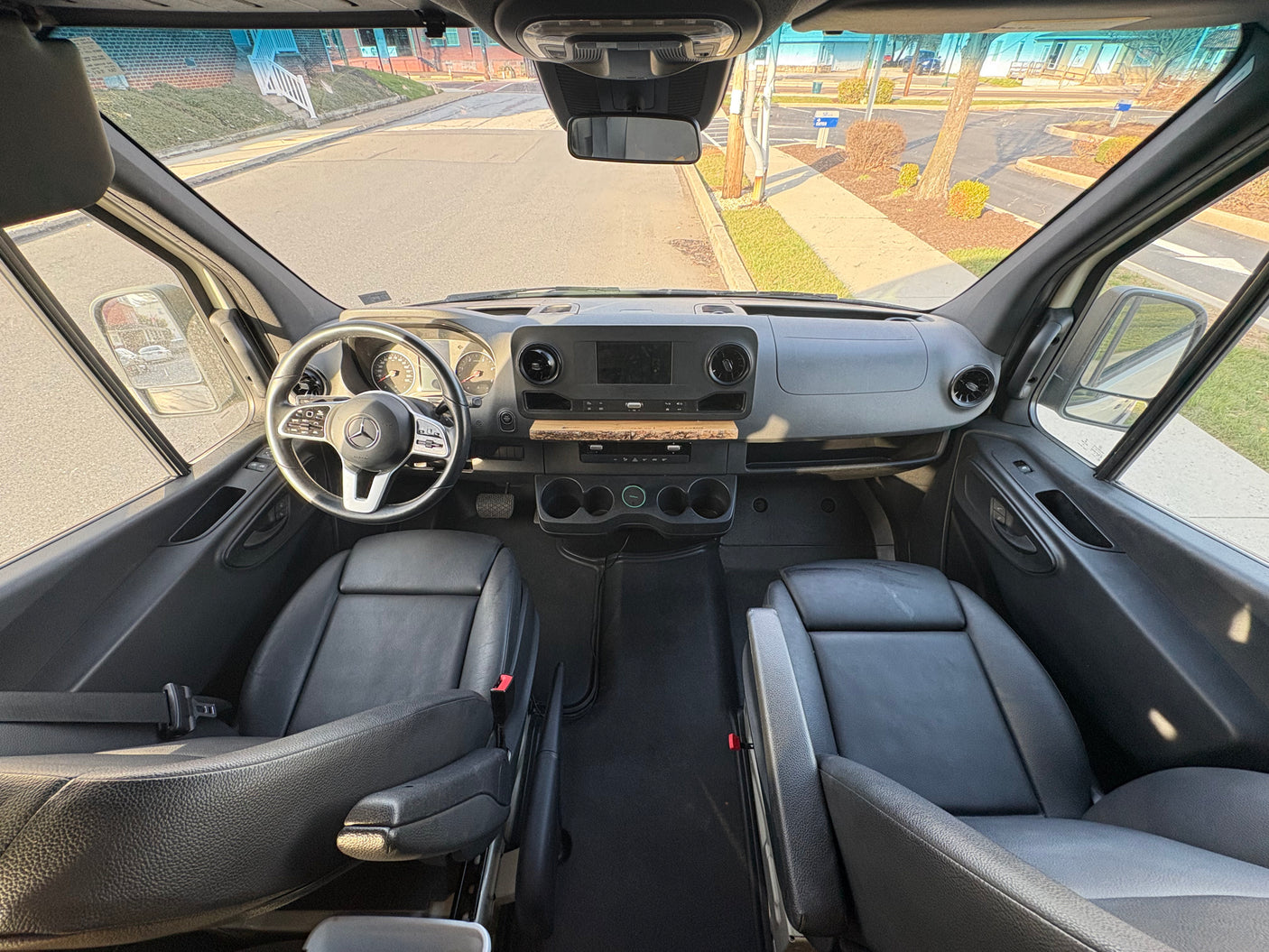 Interior of an RV rental: a Mercedes Sprinter van cockpit with black seats, dashboard, and front view of the road.