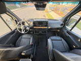 Interior of an RV rental: a Mercedes Sprinter van cockpit with black seats, dashboard, and front view of the road.