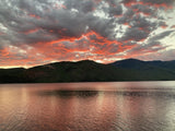 Vibrant orange and red sunset clouds reflect on a calm mountain lake, ideal for your next RV rental escape and outdoor travel.