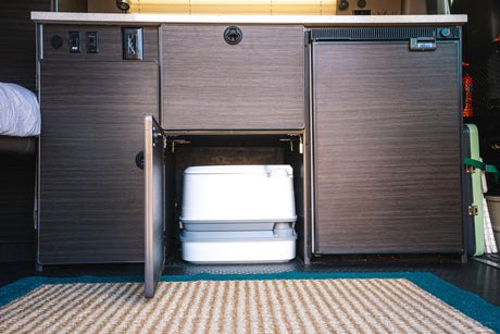 RV rental interior: organized cabinets with a portable toilet, fridge, water pump switch, & outlets. Compact travel essentials.