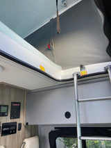 Inside an RV rental: a pop-top roof access with ladder, warning labels (crush hazard, secure), and control panels (Winnebago, solar).