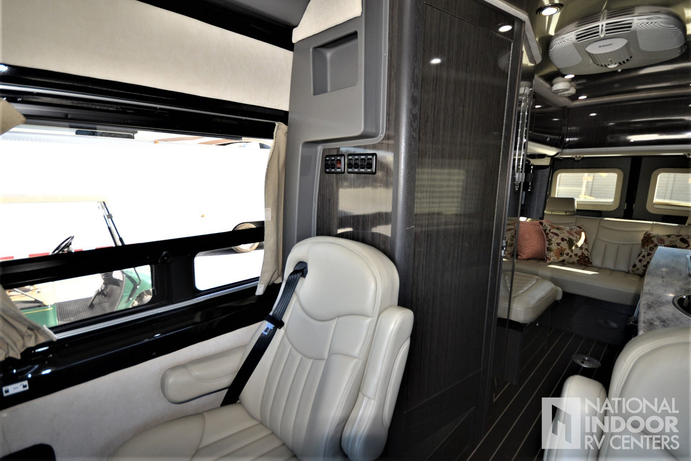 Luxury rv rental interior: cream leather seating, dark wood, Dometic AC, and large windows with outdoor view.