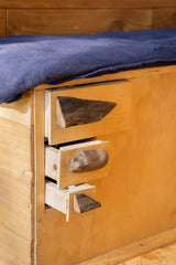 RV rental comfort: Rustic wooden drawers with unique handles integrated into a bed frame, topped with a blue blanket.