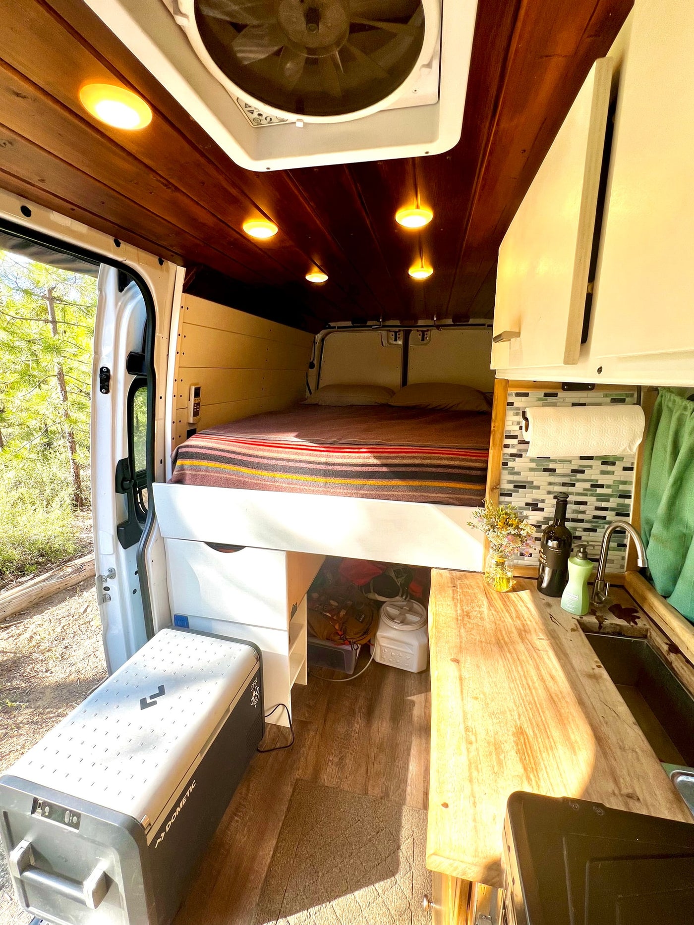 RV rental interior with a cozy bed, compact kitchen, smart storage, and natural light from the open side door. — photo 9
