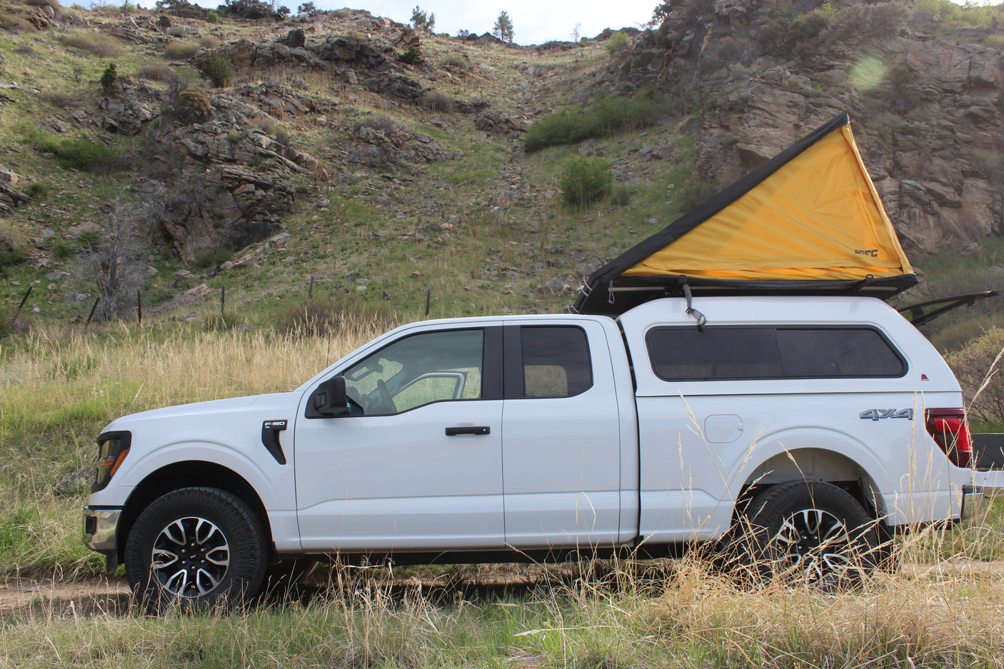 White F-150 truck, with a yellow rooftop tent & camper shell, ideal for your next rv rental adventure in nature.