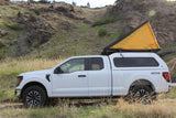 White F-150 truck, with a yellow rooftop tent & camper shell, ideal for your next rv rental adventure in nature.