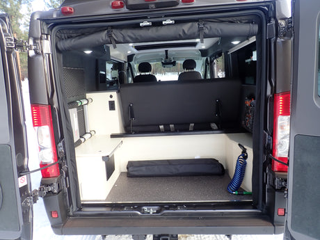 An rv rental's rear doors are open, revealing a clever, compact interior with seating, storage, and utility connections.