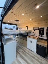 Cozy RV rental interior with raised bed, sink, fridge, and storage. Perfect for adventure.