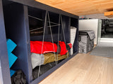Custom RV rental storage: dark blue shelves with bungee cords organize camping gear, blue blocks, and a cooler on light wood floors.
