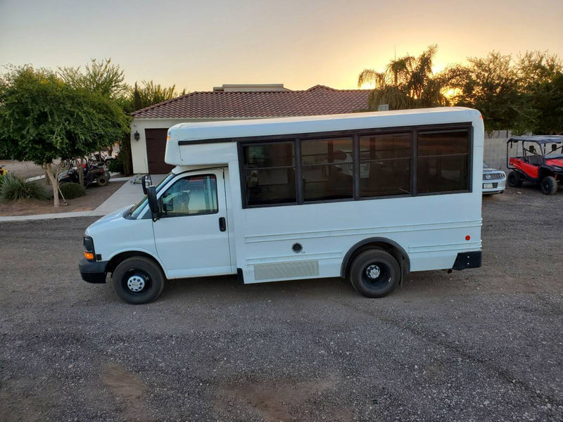 This white shuttle bus, ideal for an RV rental conversion, is parked on gravel at sunset. — photo 1